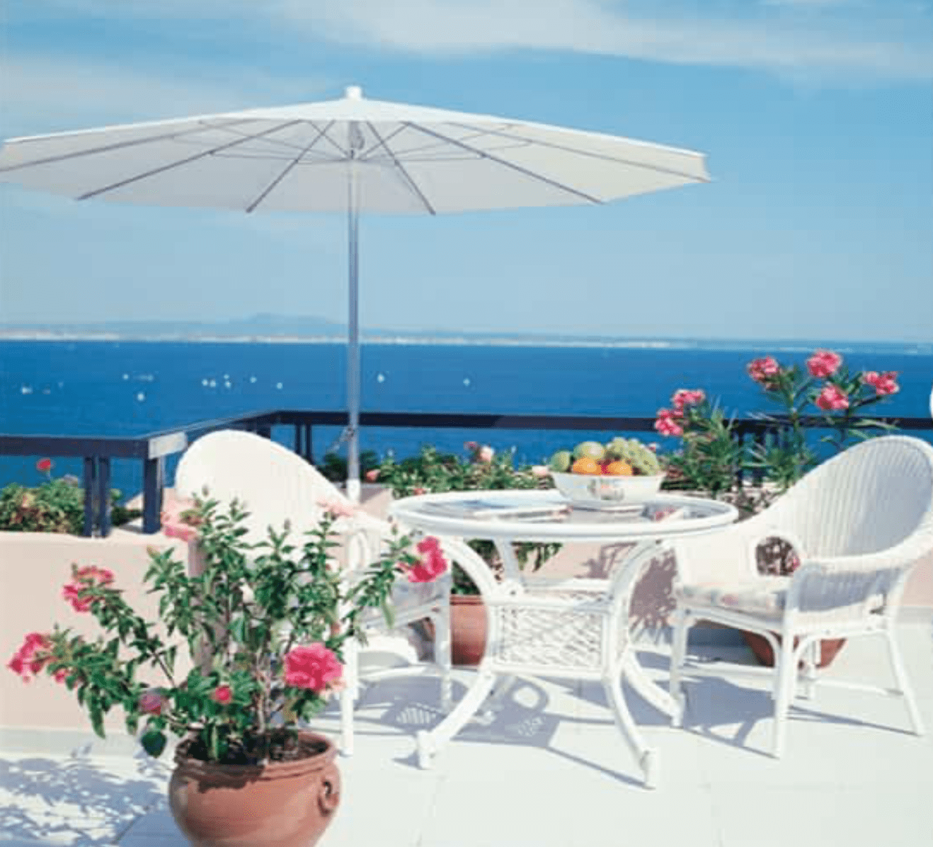 white outdoor table for two with umbrella with an ocean view