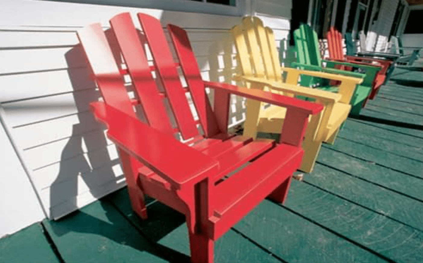 red chair and yellow chair and other multi colored chairs on green porch and white house