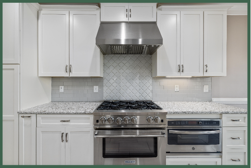 A finished kitchen with white cabinets, marble countertop, and silver appliances.